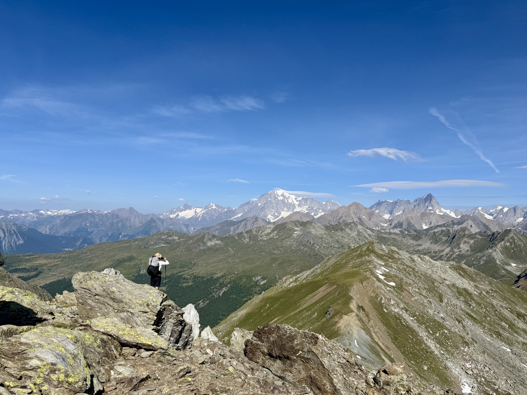Personne debout sur un rocher, vue panoramique sur montagnes et ciel bleu dégagé.