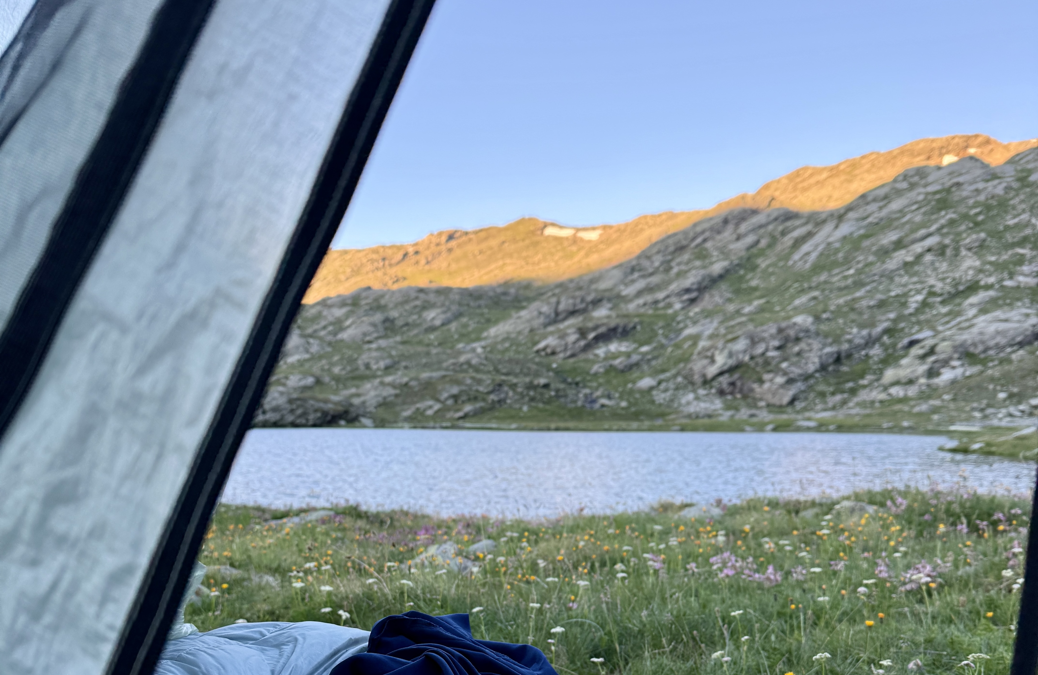 Vue depuis une tente sur un lac alpin entouré de montagnes au lever du soleil.