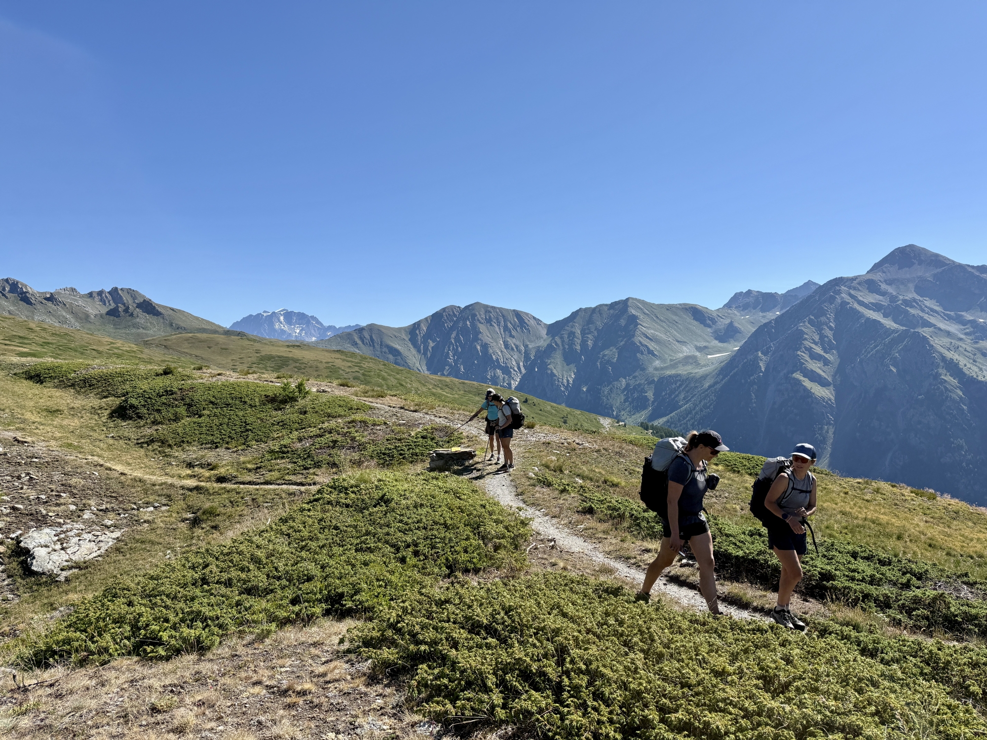 Des randonneurs sur un sentier de montagne avec un ciel bleu et des sommets en arrière-plan.