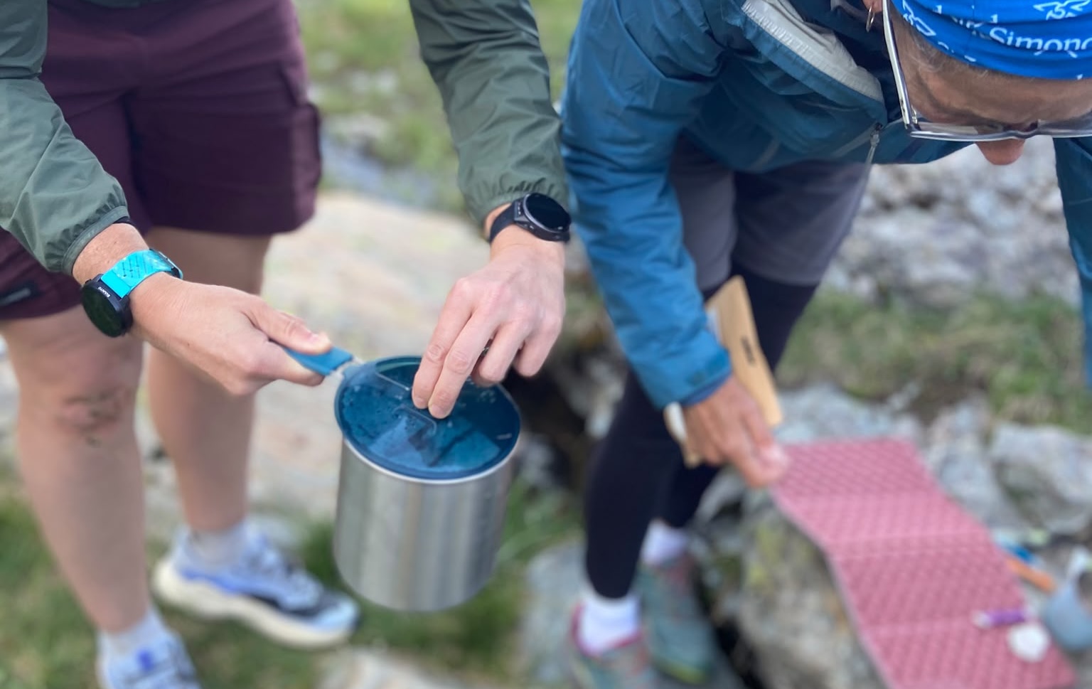 Deux personnes en plein air utilisant un récipient métallique avec un couvercle bleu.