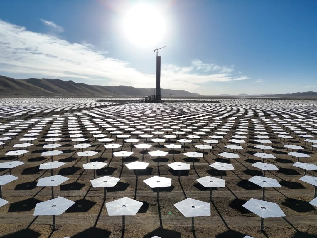 Tour solaire entourée d'héliostats dans un désert sous un ciel ensoleillé et nuageux.