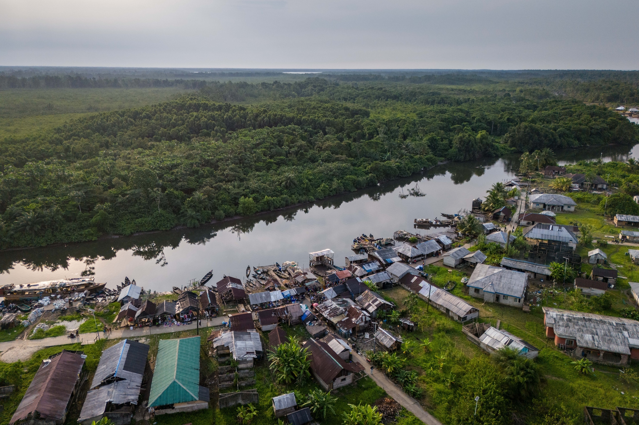 Village au bord d'une rivière entourée de forêt tropicale, maisons en bois et verdure.