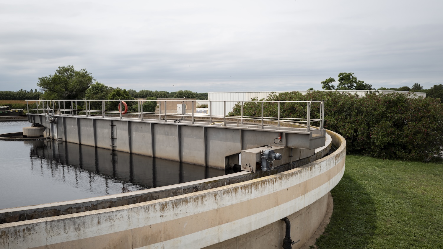 Installation de traitement des eaux usées avec réservoir circulaire et végétation environnante sous ciel nuageux