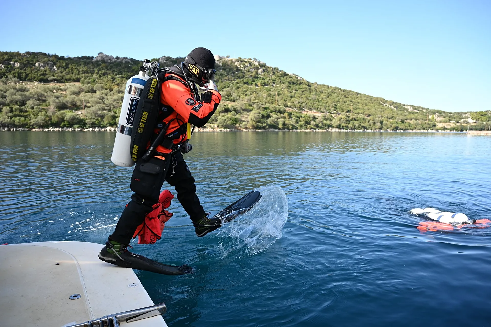 Un plongeur équipé saute dans l'eau depuis un bateau, une personne flotte à proximité.