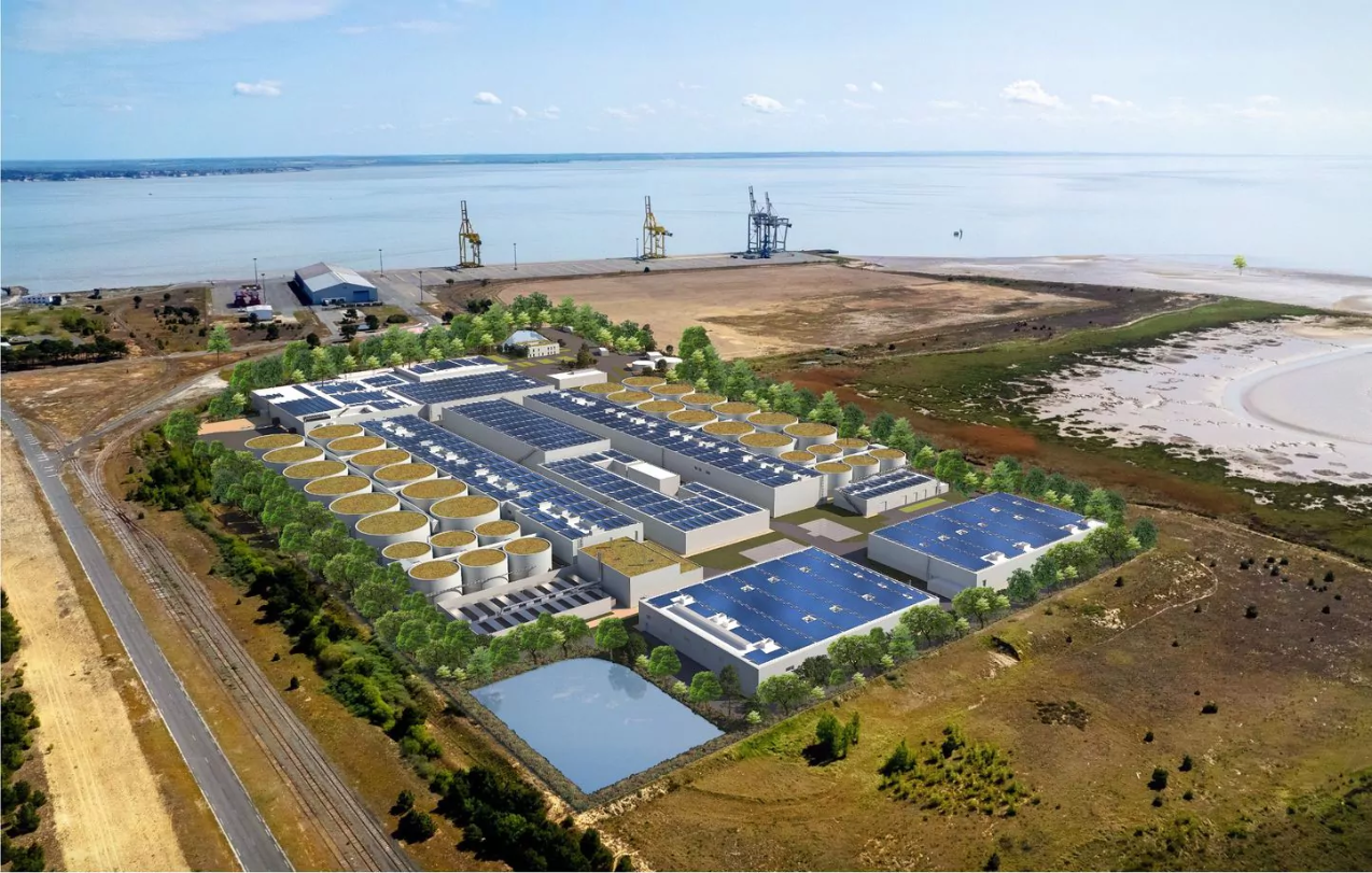 Vue aérienne d'une usine moderne en bord de mer avec panneaux solaires et infrastructures portuaires.