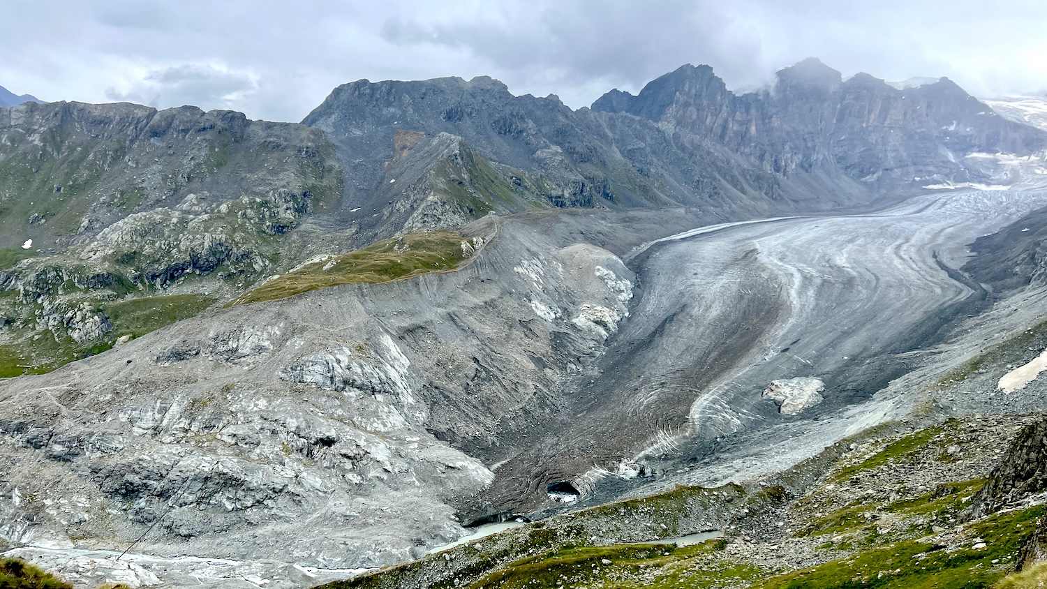 Glacier de montagne entouré de sommets rocheux sous un ciel nuageux.