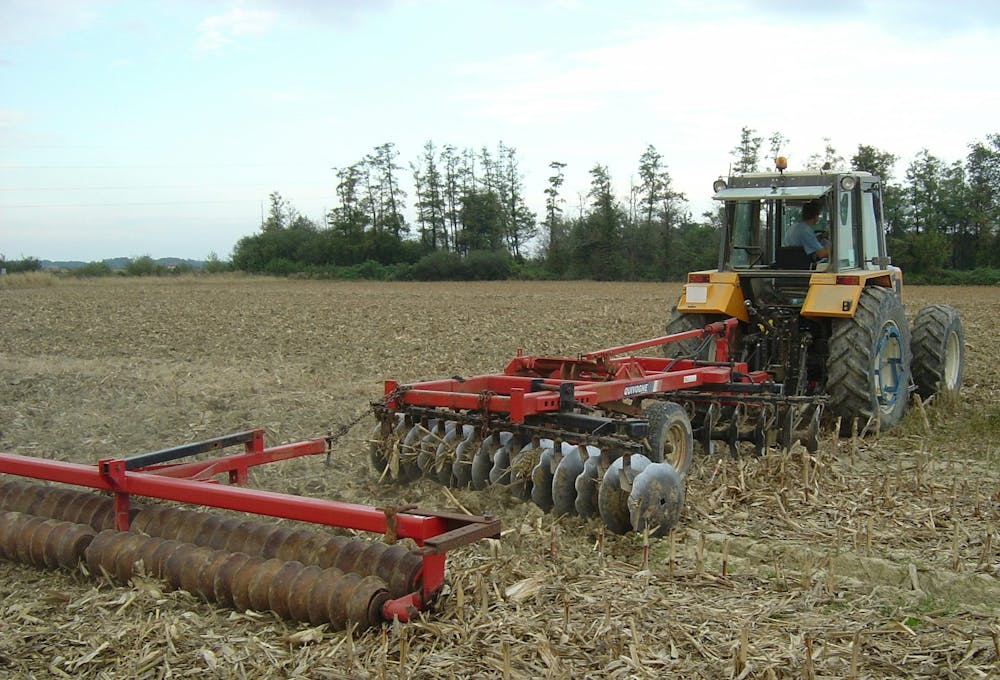 Un tracteur labourant un champ avec une herse à disques et un rouleau.