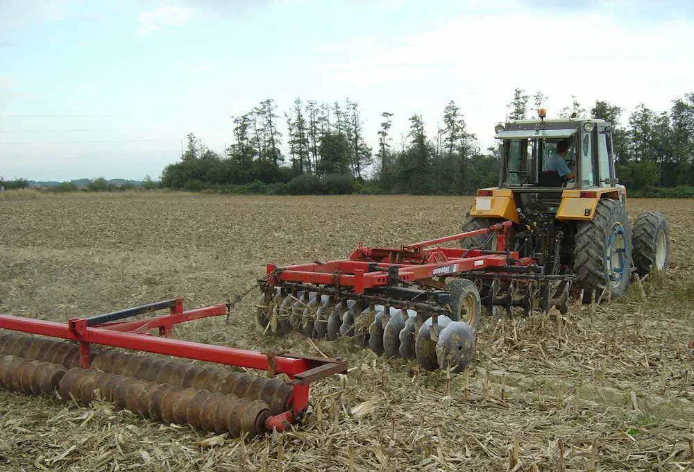 Un tracteur labourant un champ avec une herse à disques et un rouleau.