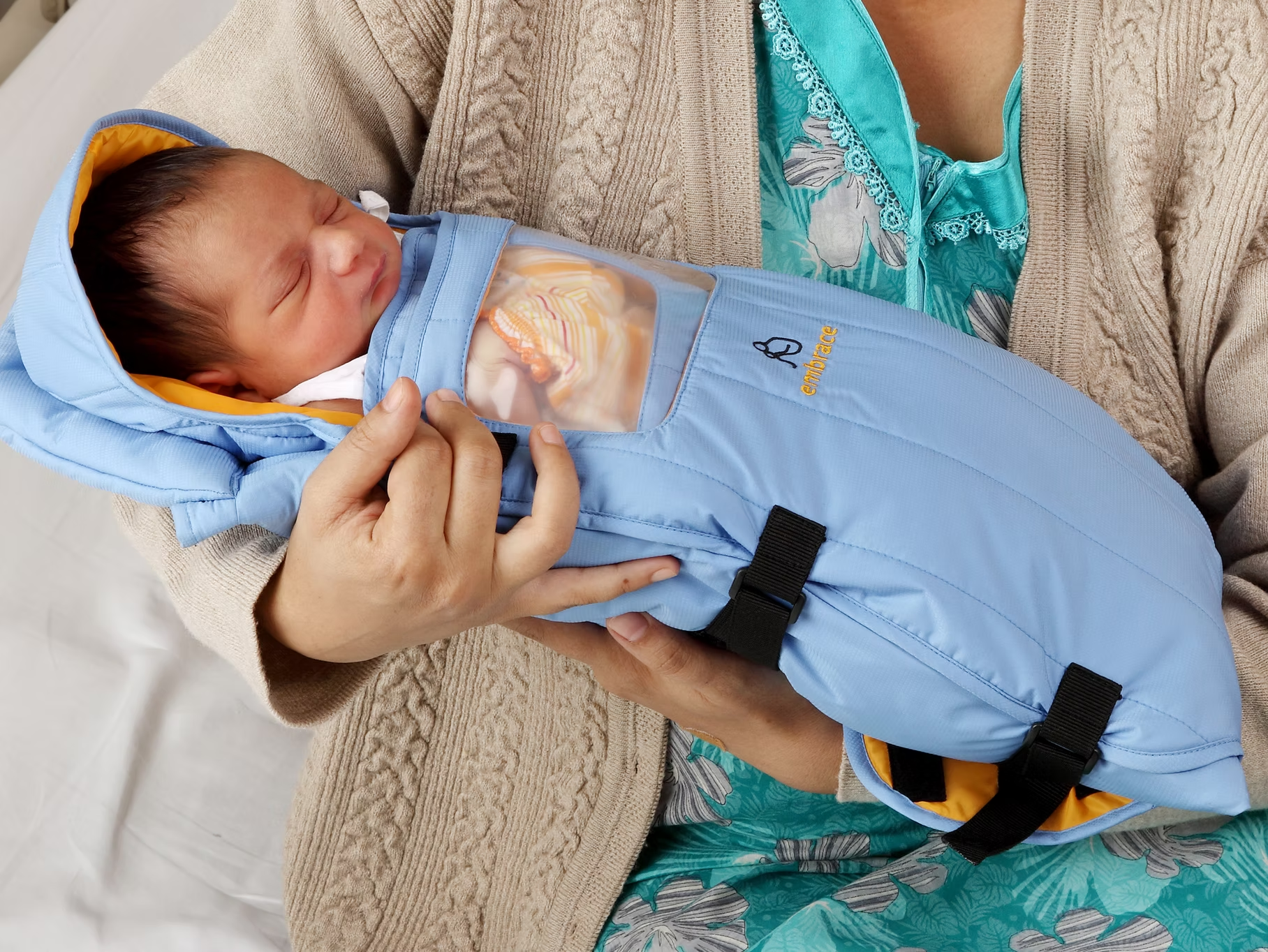 Bébé emmailloté dans une couverture bleue, tenu par un adulte, avec soin et tendresse.