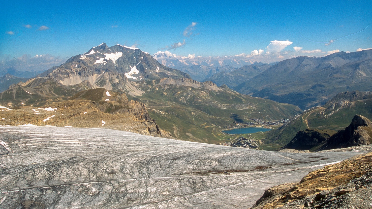 Vue panoramique sur les montagnes enneigées avec un glacier au premier plan et un lac.
