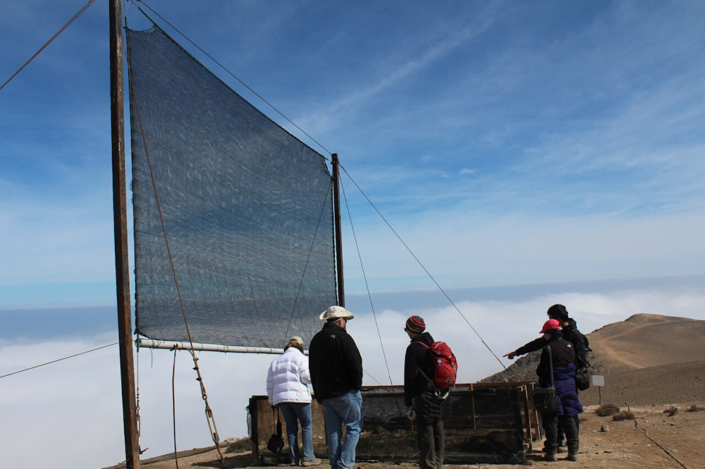 Personnes observant un filet à brouillard sur une montagne sous un ciel bleu.