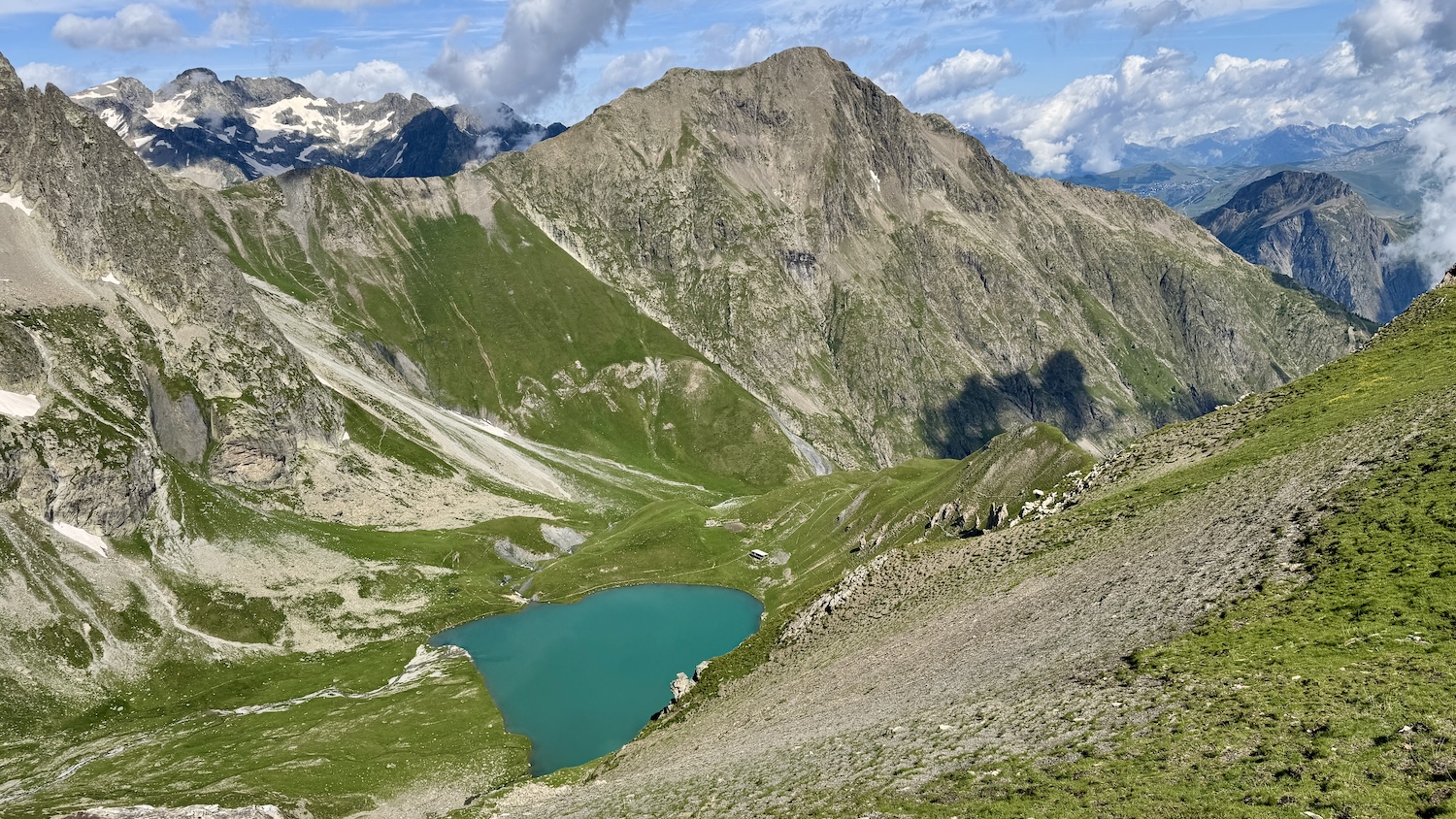 Lac alpin entouré de montagnes verdoyantes sous un ciel partiellement nuageux.