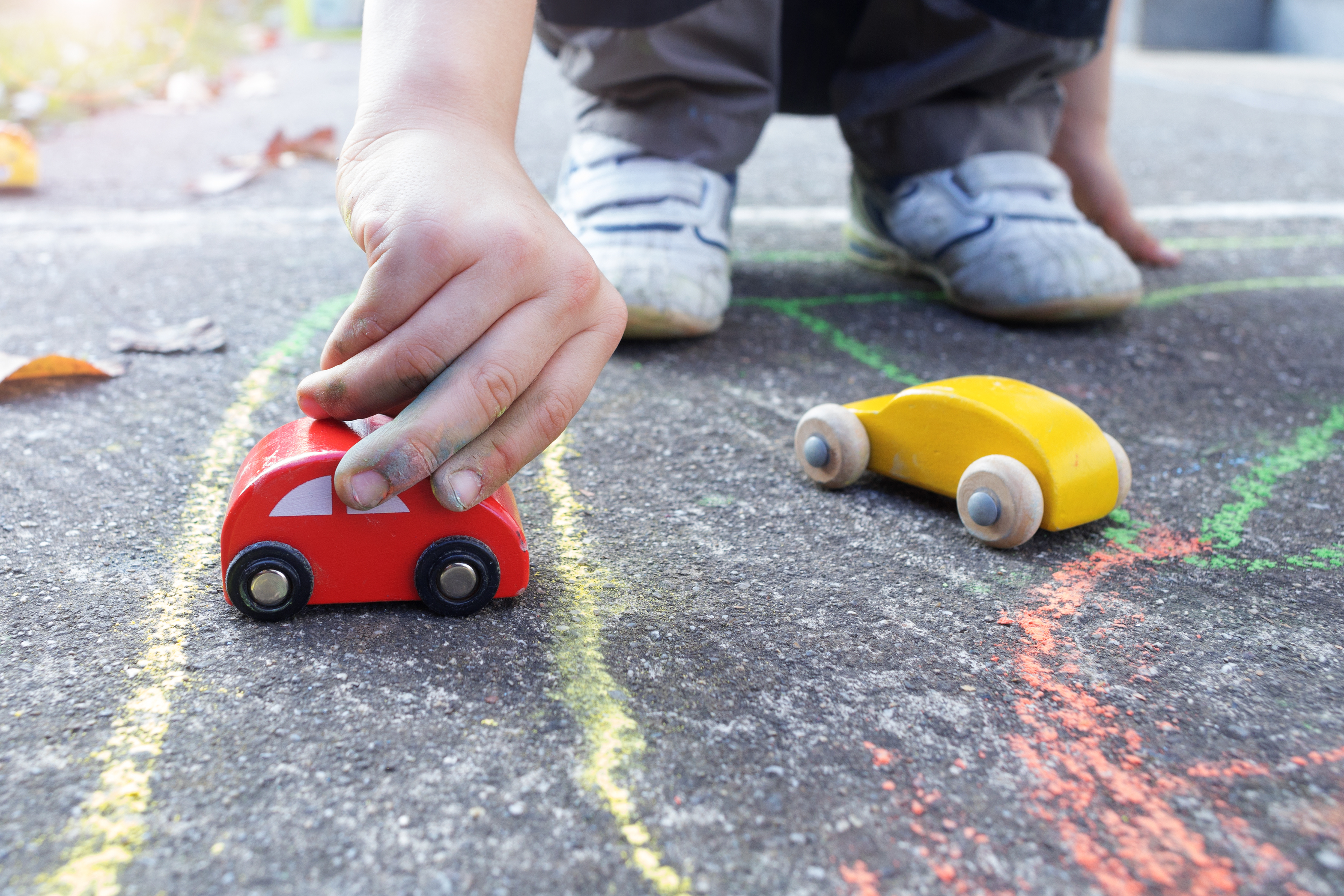 Enfant jouant avec des voitures en bois sur un trottoir décoré de dessins à la craie.