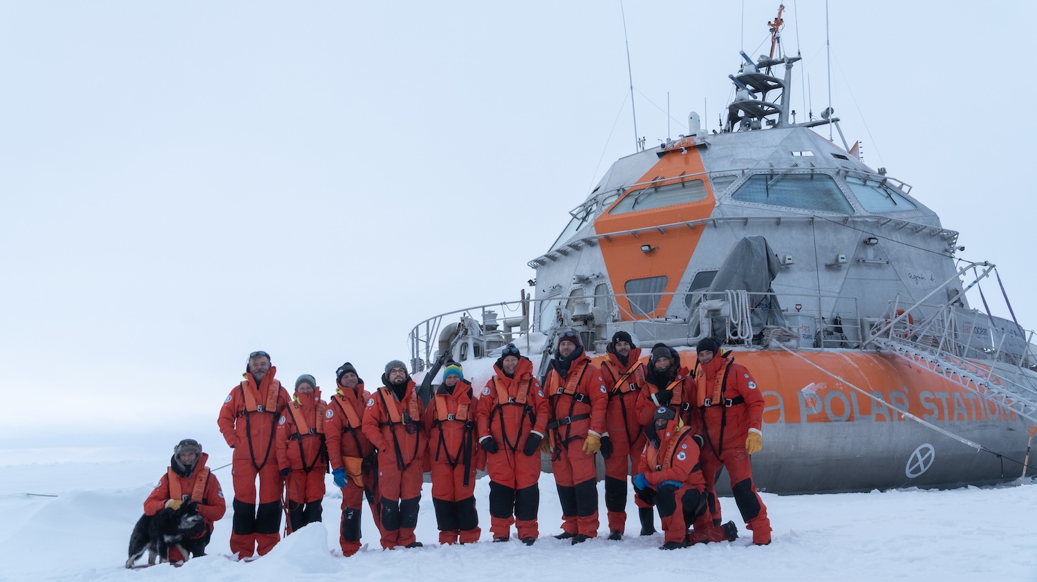 Un groupe en combinaisons orange devant un navire de la Garde côtière dans la neige.