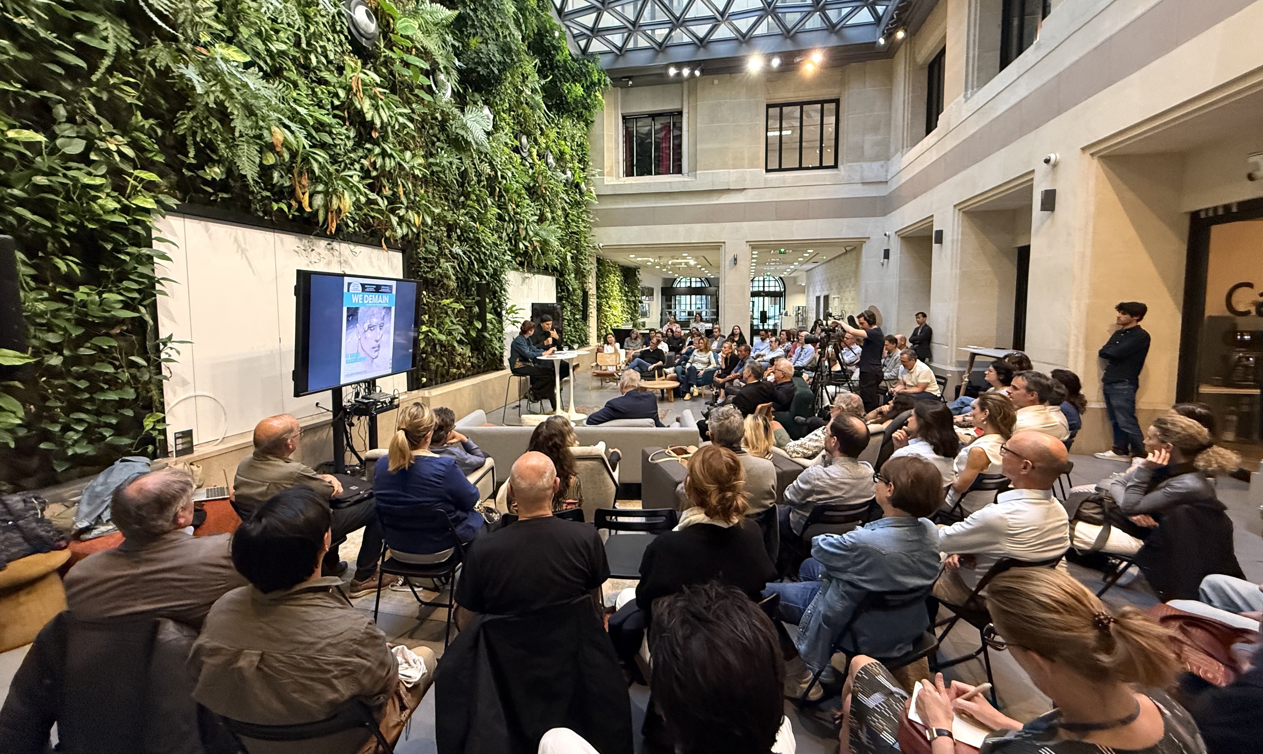 Conférence dans un espace moderne avec un mur végétal et une audience attentive.