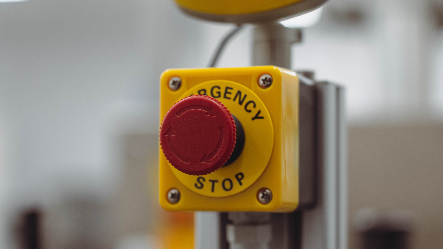 Bouton d'arrêt d'urgence rouge sur fond flou dans un environnement industriel.