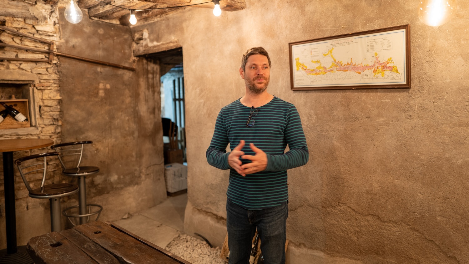 Un homme debout dans une pièce rustique avec des murs en pierre et des luminaires suspendus.