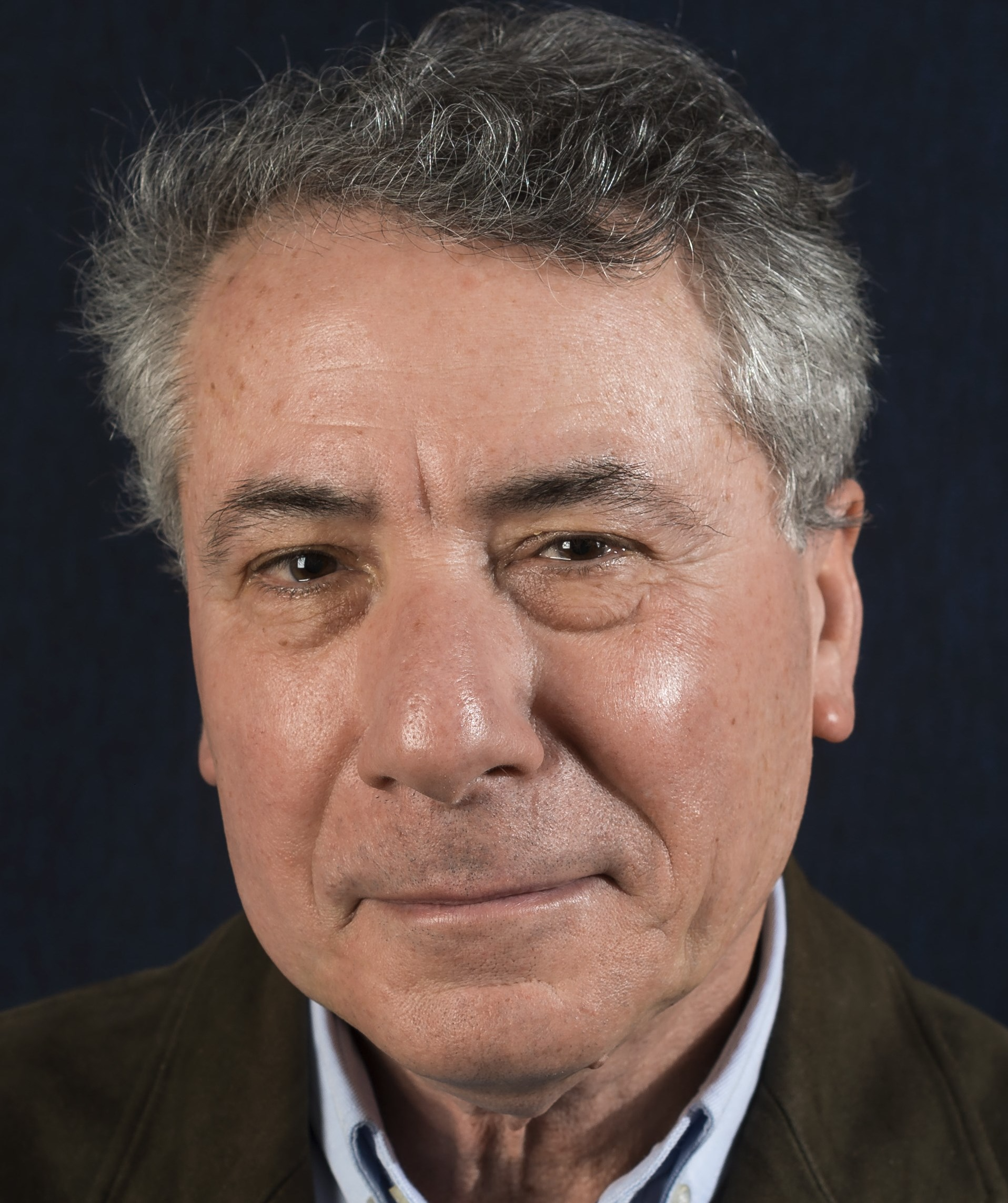 Portrait d'un homme aux cheveux gris sur fond sombre, portant une veste.