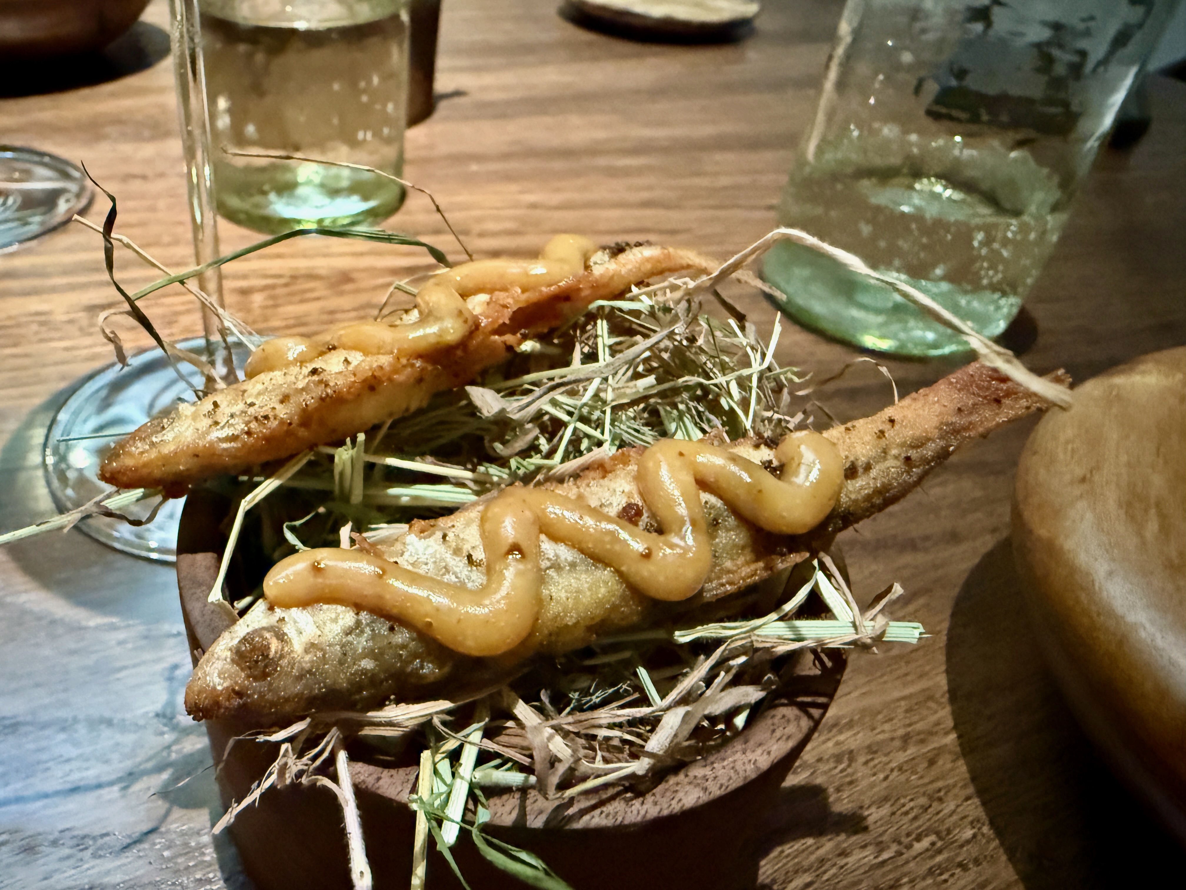 Des racines garnies d'une sauce, présentées sur un lit de foin, sur une table en bois.