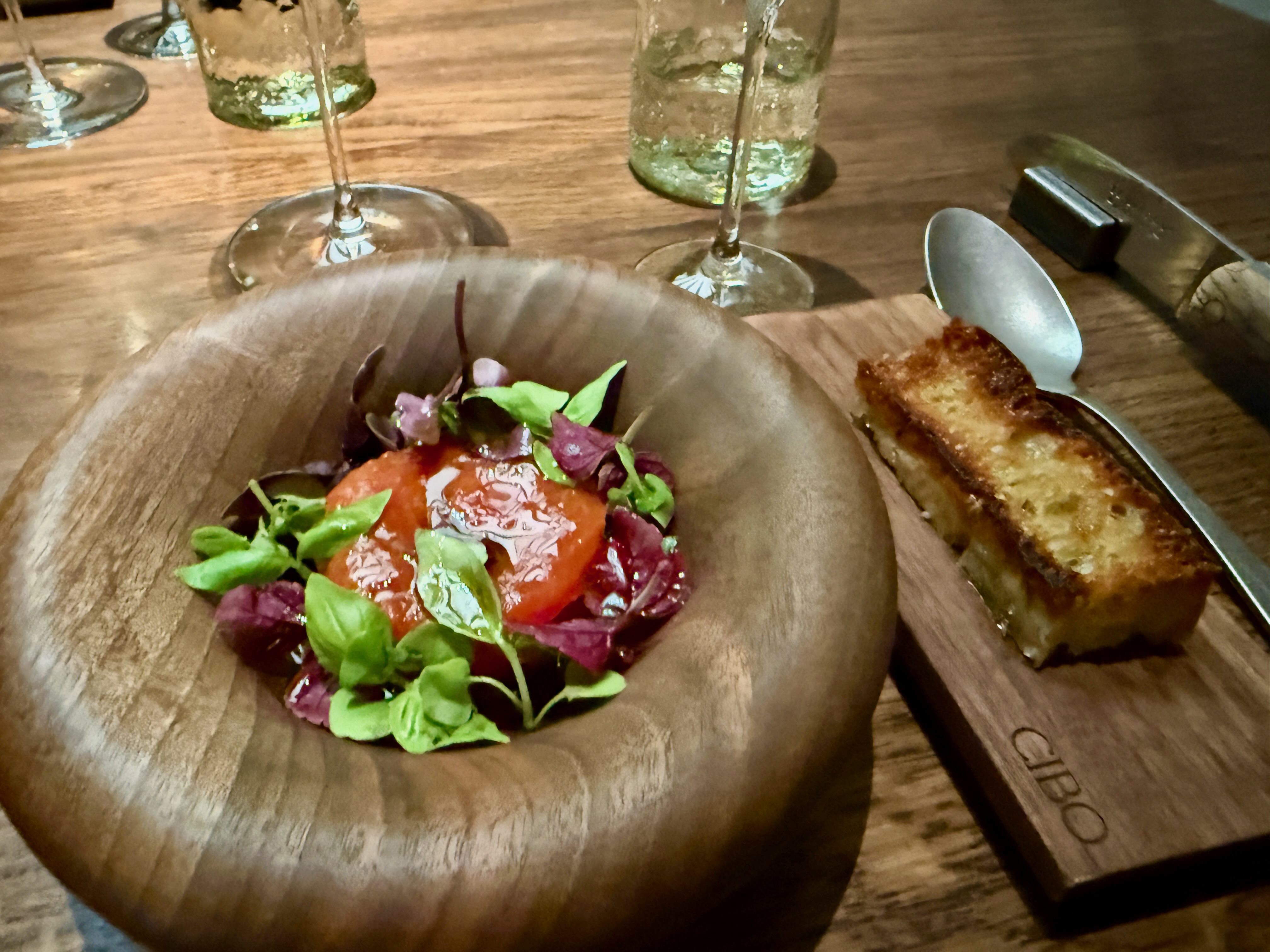 Salade colorée dans un bol en bois avec accompagnement de pain grillé et verres de vin.